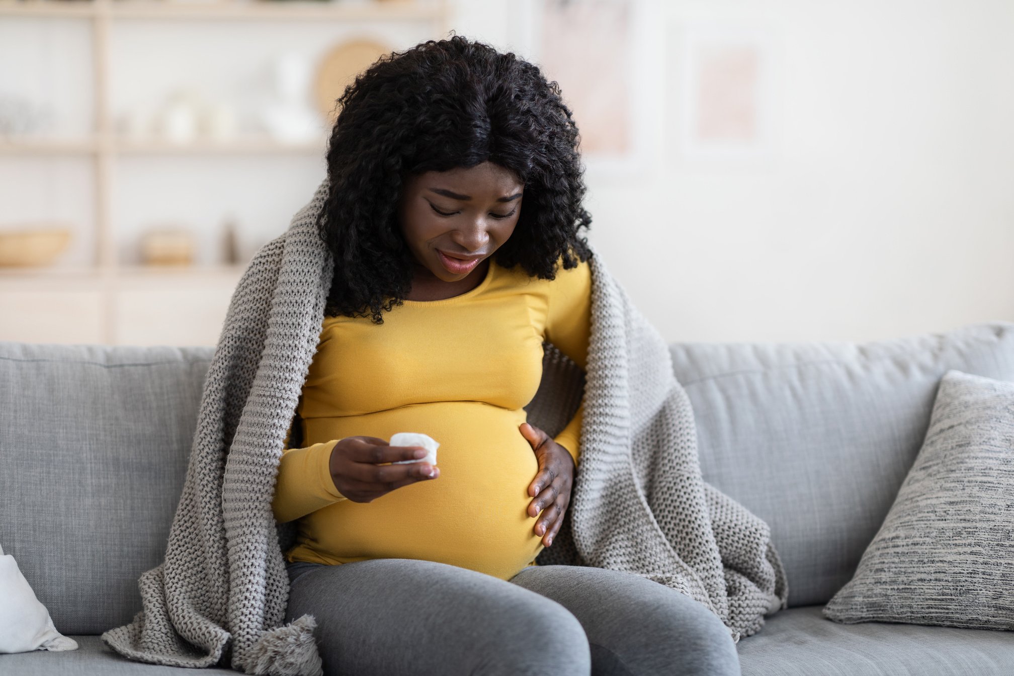 Pregnant black woman covered in blanket feeling sick